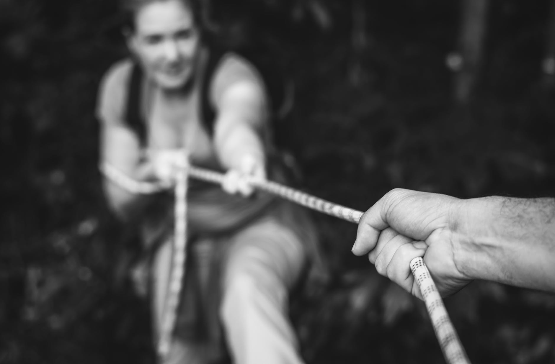 grayscale photo of person pulling up woman using rope